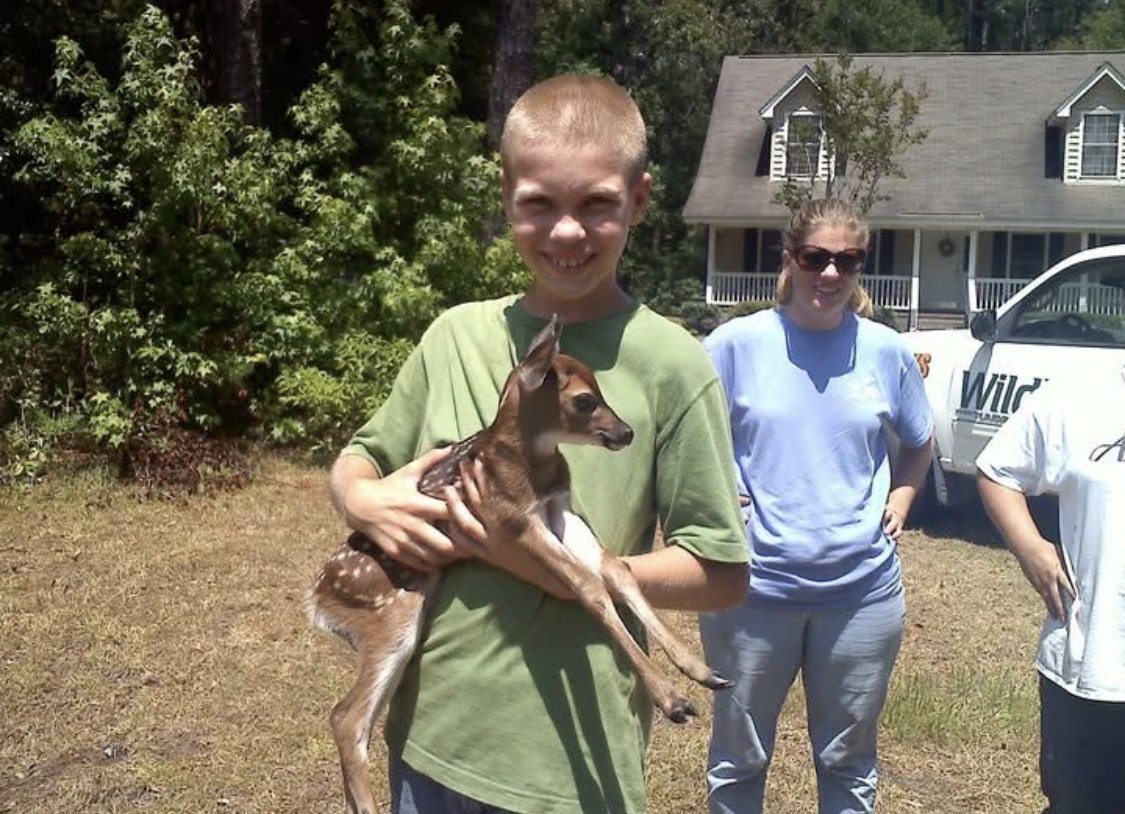 Young Evan holding a rescued fawn outdoors